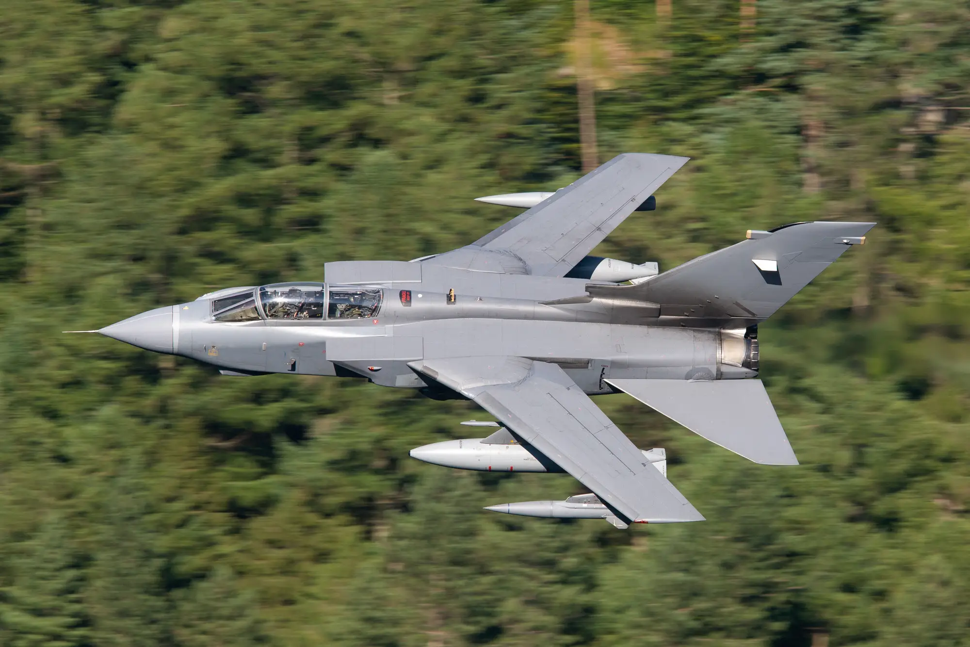 An RAF Tornado jet banking low and fast against a blurred forested hillside